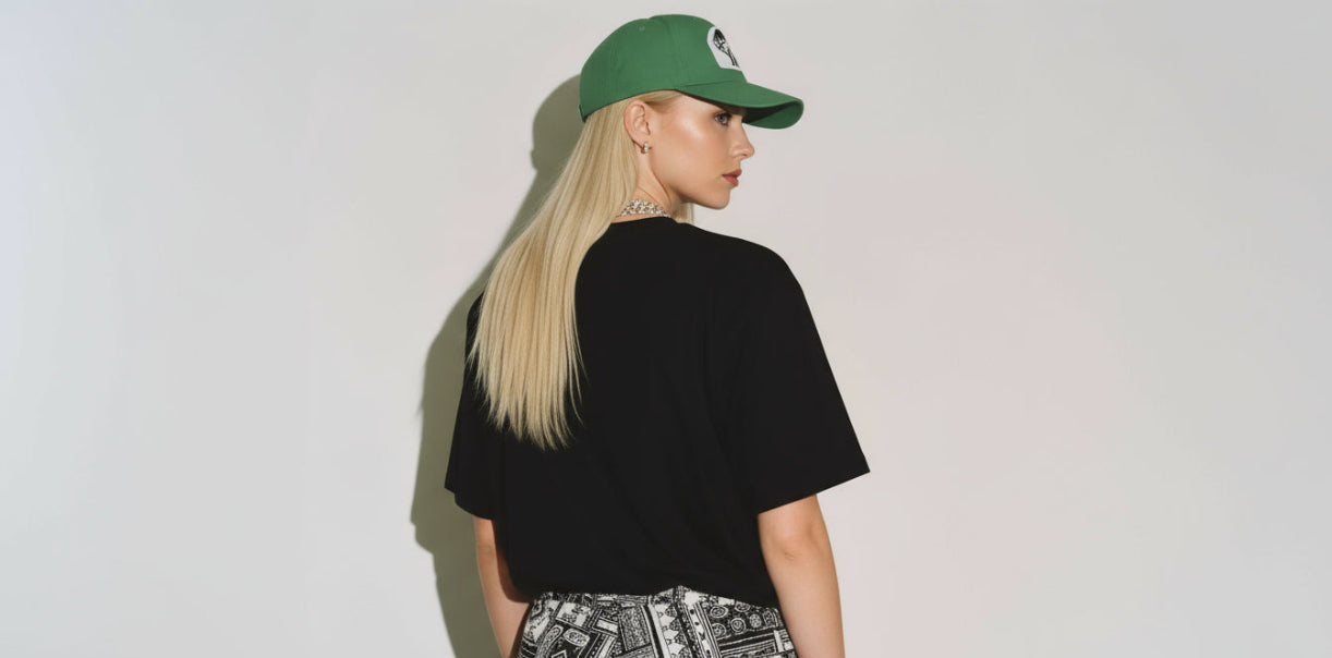 Person wearing a black t-shirt, patterned pants, and a green cap on a plain background
